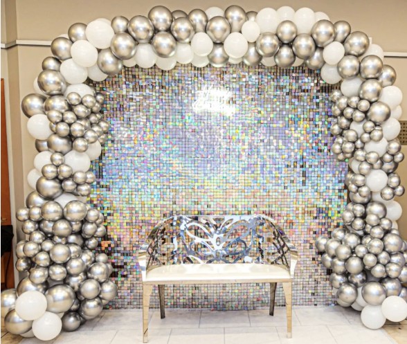 Silver and white balloon arch framing a sequin backdrop and gold bench