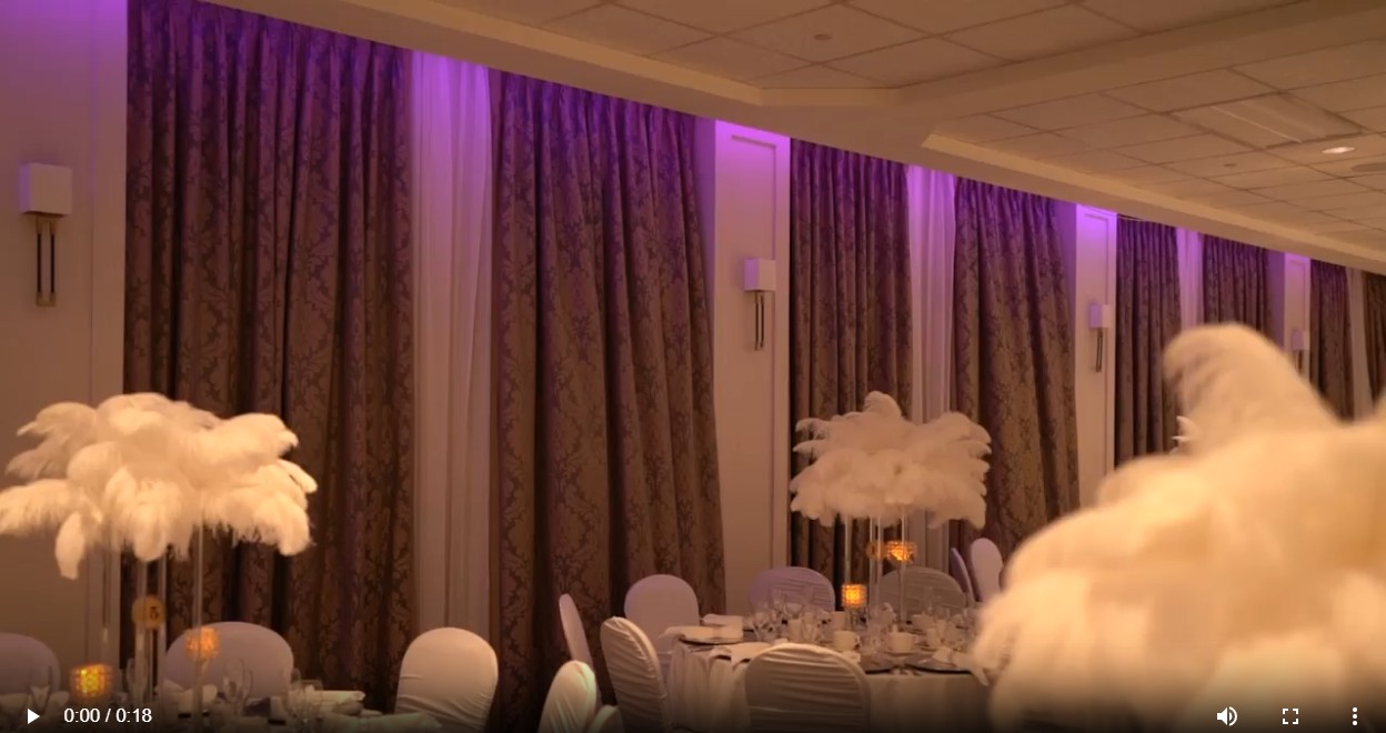 Ballroom reception styled with uplighting, draped curtains and feather centerpieces